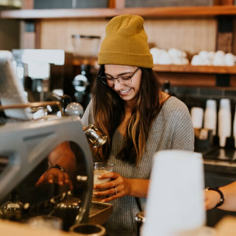 Barista in a yellow hat making coffee drinks in a cozy cafe